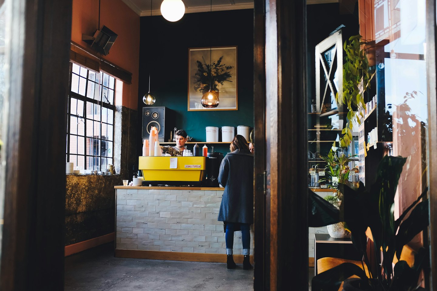 Barista making coffee at a yellow espresso machine inside a cafe.